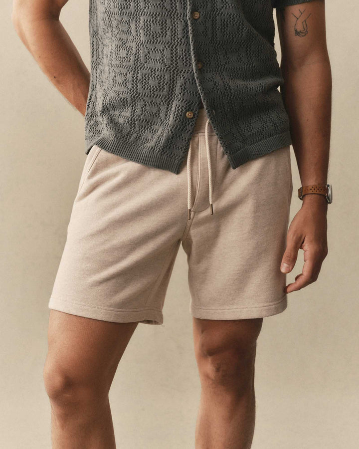 Person wearing Taylor Stitch Sunset Shorts in Heather Oat Terry and a dark knitted cardigan on a neutral background