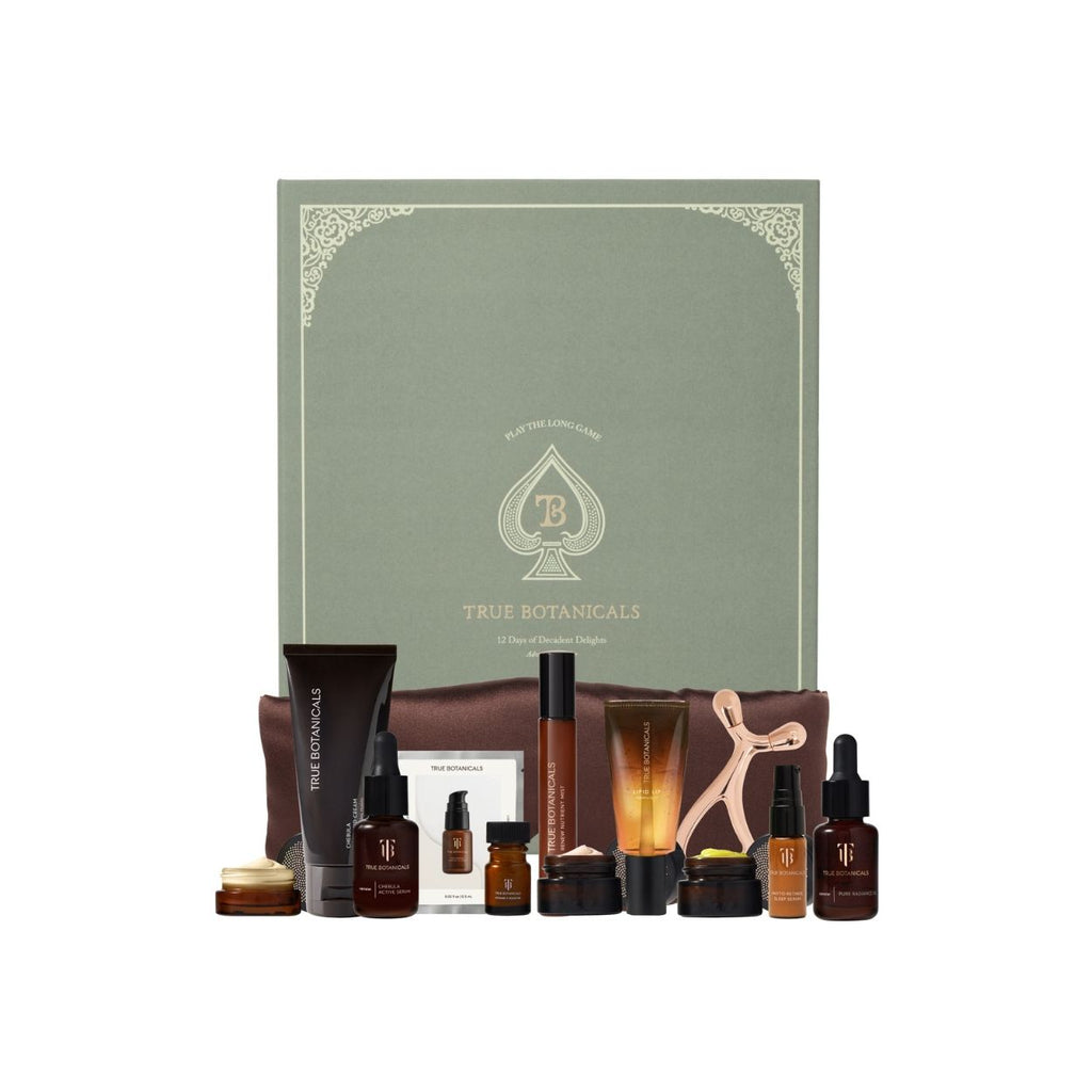 True Botanicals skincare gift set featuring a sage green gift box with gold detailing, a brown cosmetic pouch, and multiple skincare bottles and jars in amber, black, and rose gold tones, arranged on a white background.