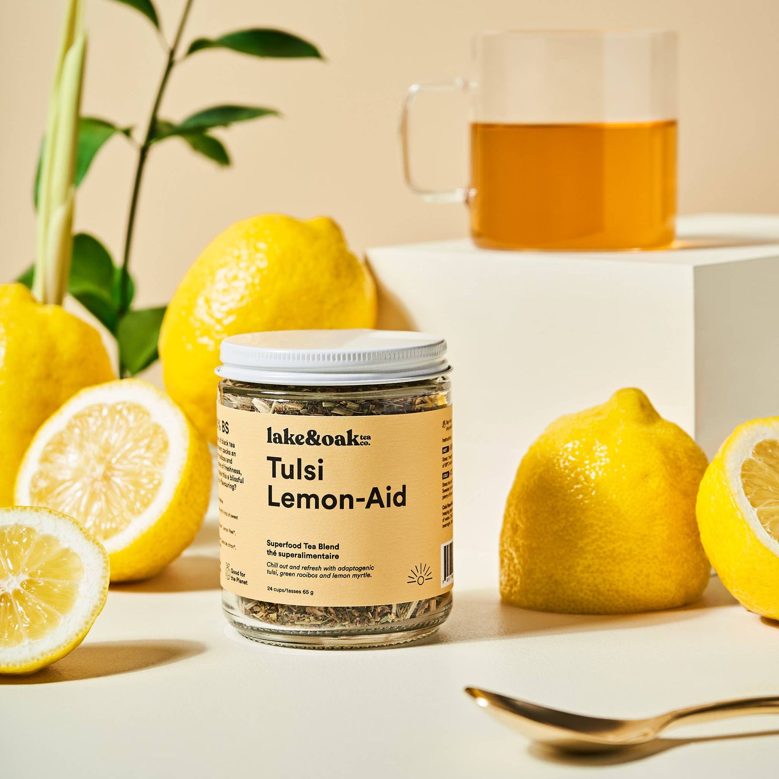 Jar of lake&Oak Tulsi Lemon Aid with lemons and a glass of tea on a light background