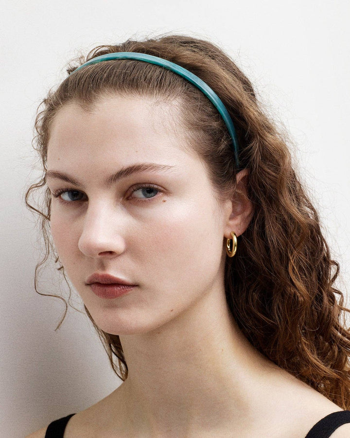 Woman with wavy hair wearing a teal headband against a plain background