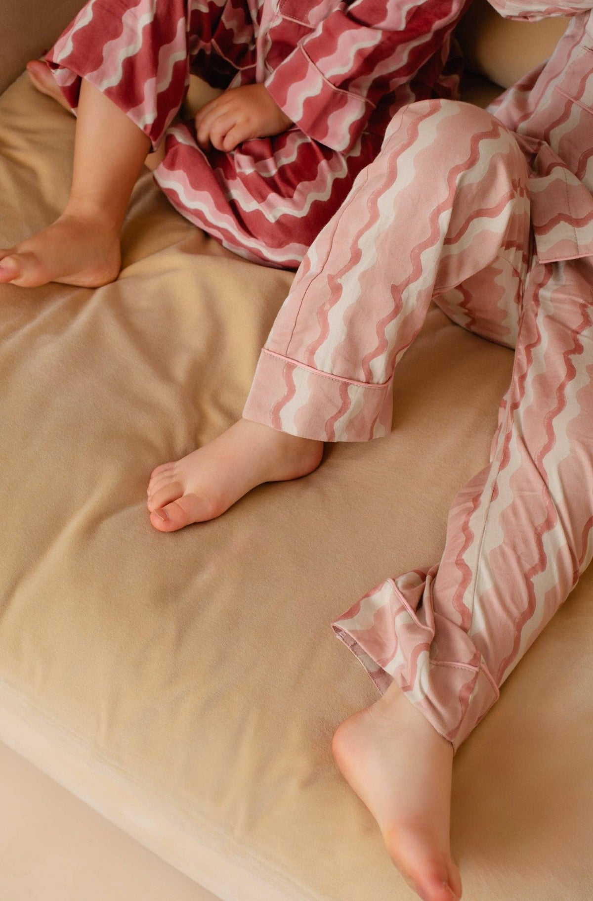 Children wearing pink and white pajamas sitting on a beige surface.
