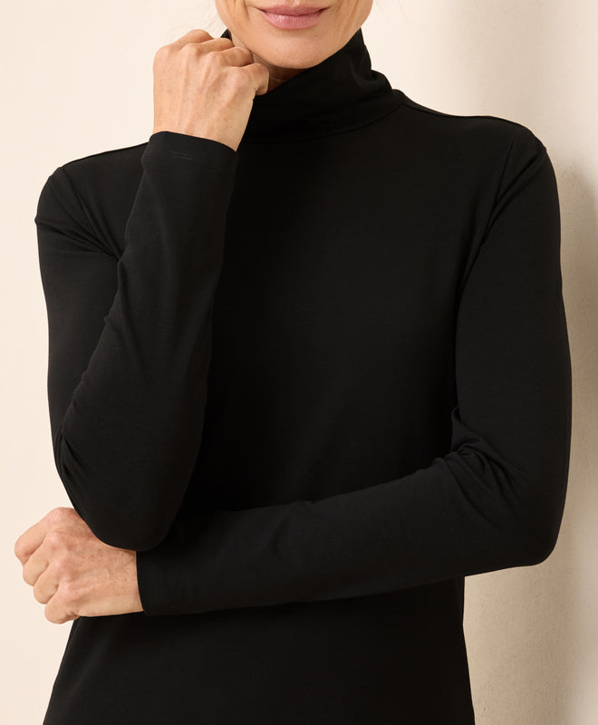 Person wearing a black turtleneck sweater against a beige background
