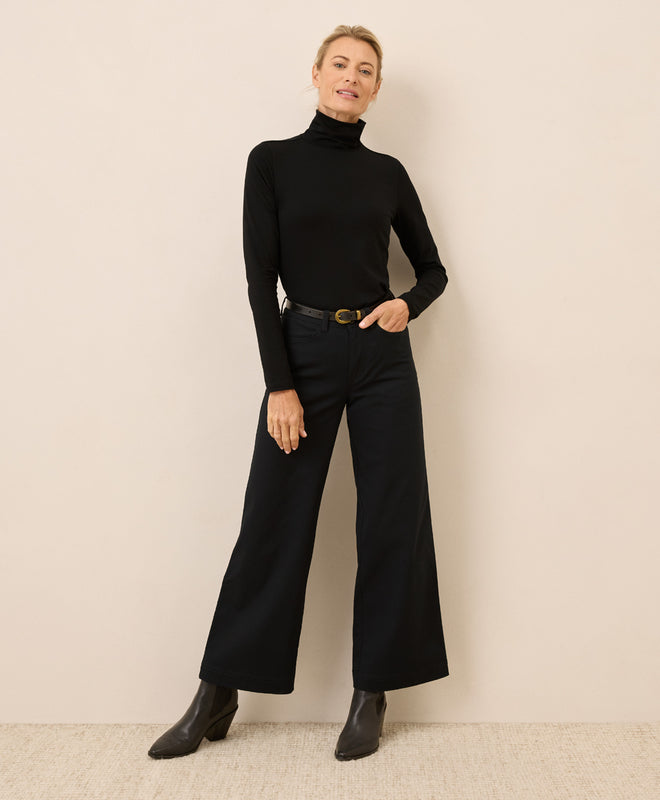 Woman wearing a black turtleneck and wide-leg pants against a beige background