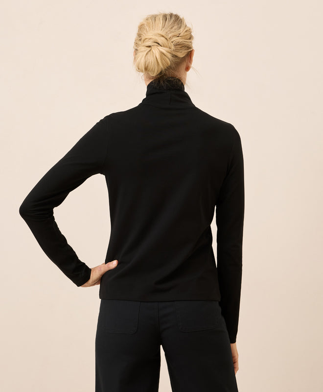 Person wearing a black long-sleeve top against a beige background