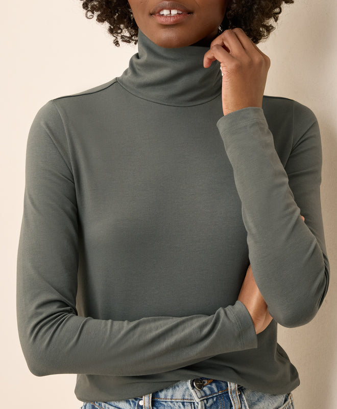 Person wearing a castor green turtleneck sweater against a neutral background