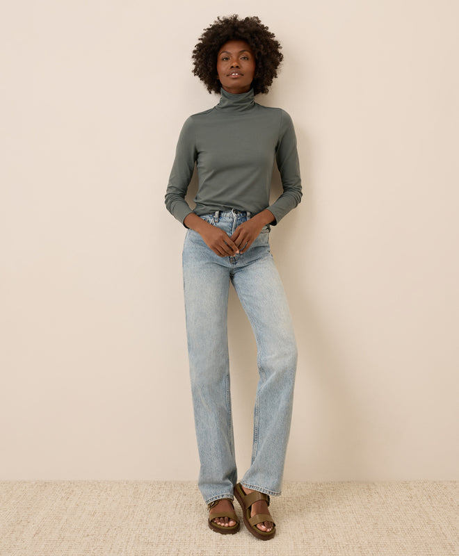 Person wearing a castor green turtleneck and light blue jeans against a beige background