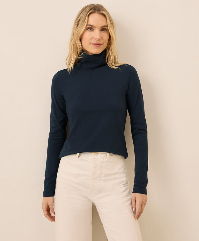 Woman wearing a navy blue long-sleeve top and white pants against a beige background