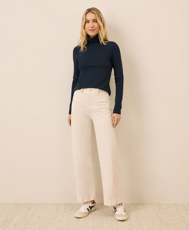 Woman wearing a navy turtleneck and beige pants against a beige background