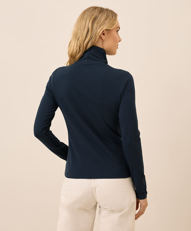 Woman wearing a navy blue long-sleeve top against a beige background
