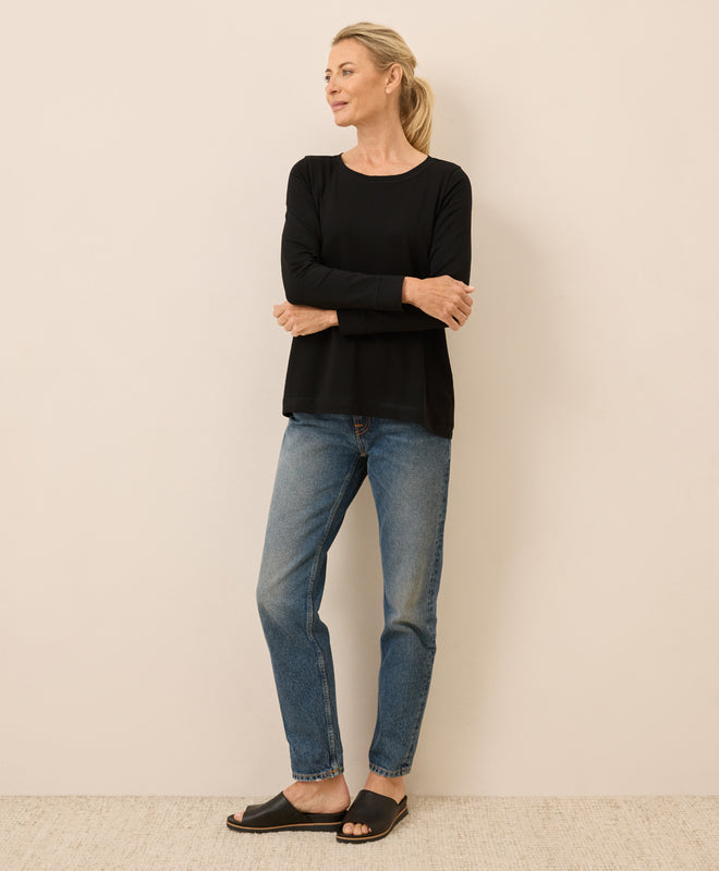 Woman wearing a black top and blue jeans against a plain background
