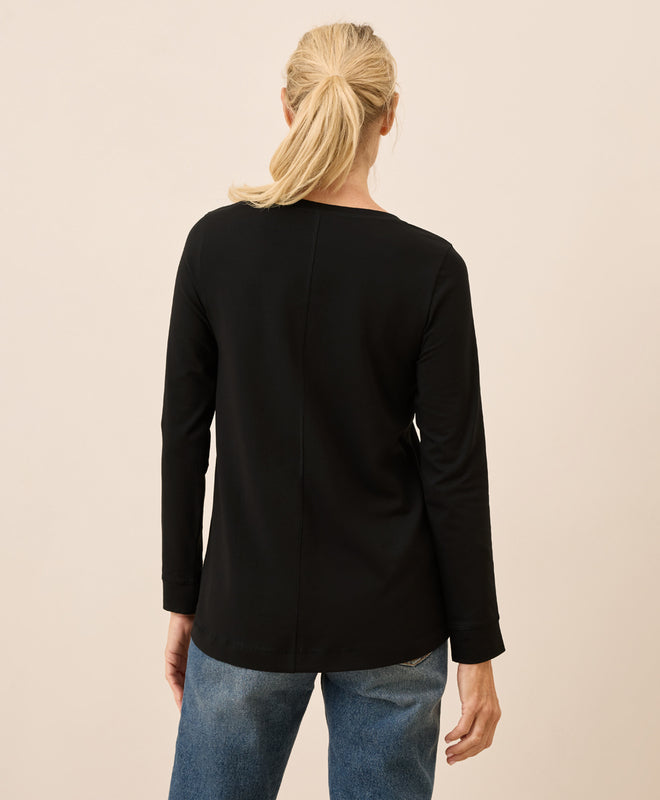 Person wearing a black long-sleeve top and blue jeans on a beige background