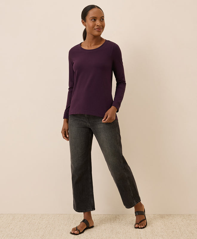 Woman wearing a purple long-sleeve top and dark jeans on a beige background