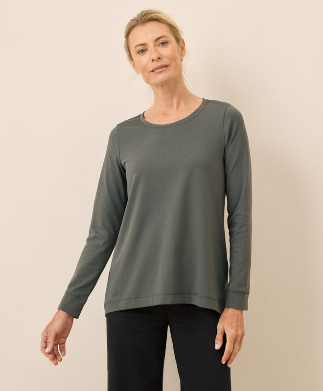 Woman wearing a green long-sleeve top against a beige background