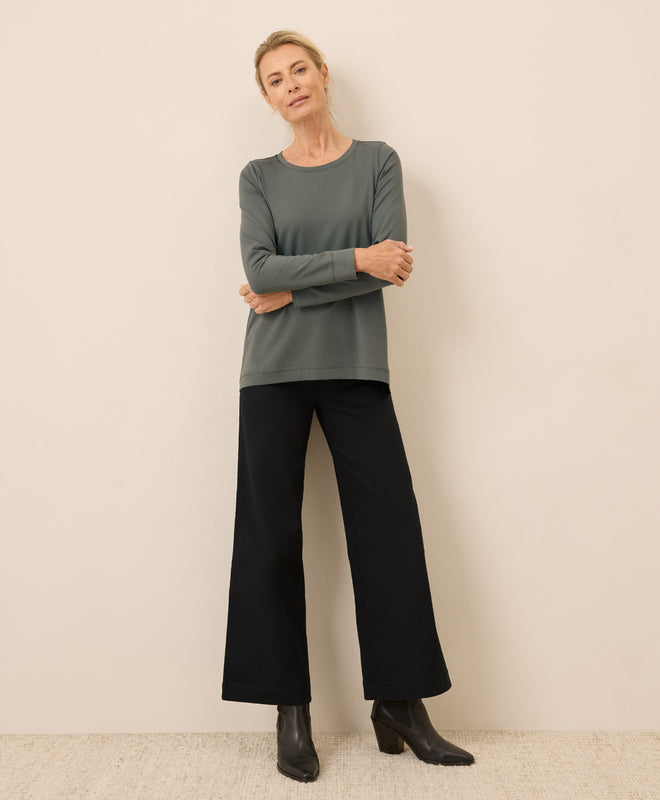 Woman wearing a green long-sleeve top and black pants against a beige background