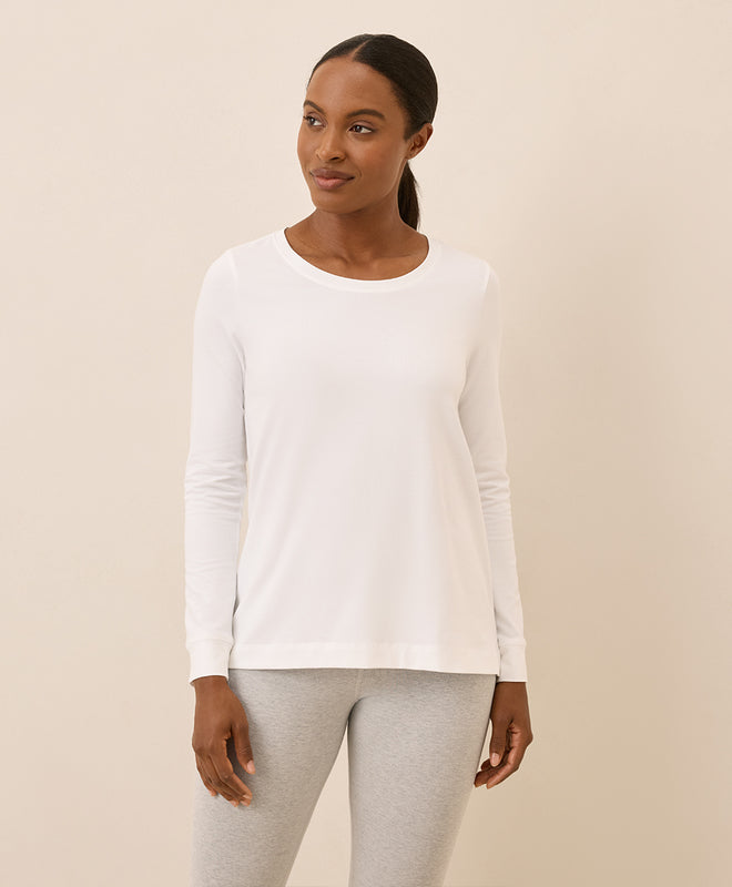 Woman wearing a white long-sleeve top and gray leggings on a beige background