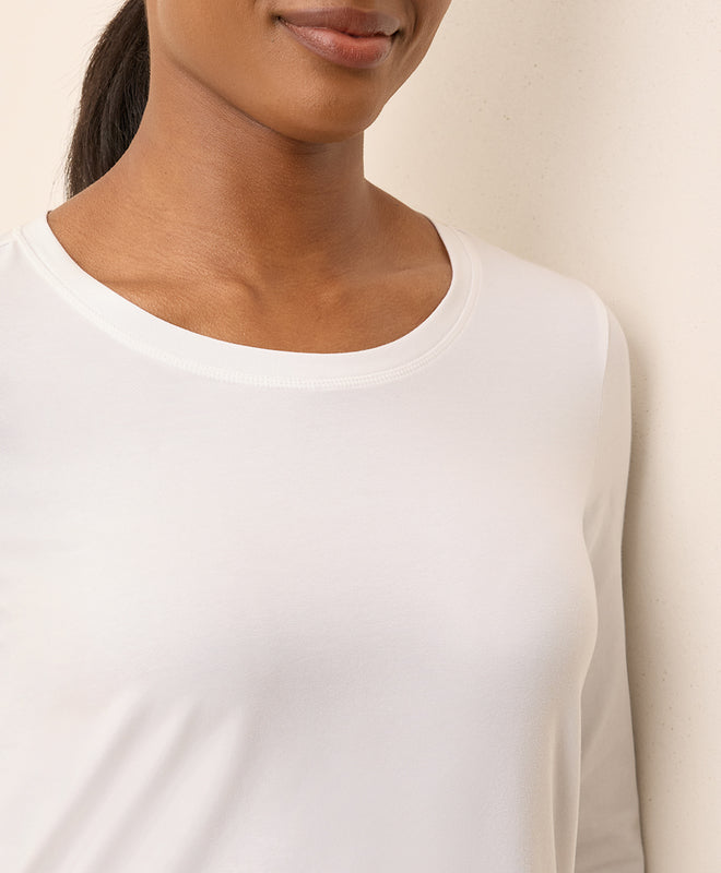Close-up of a women wearing a plain white long-sleeve shirt against a neutral background