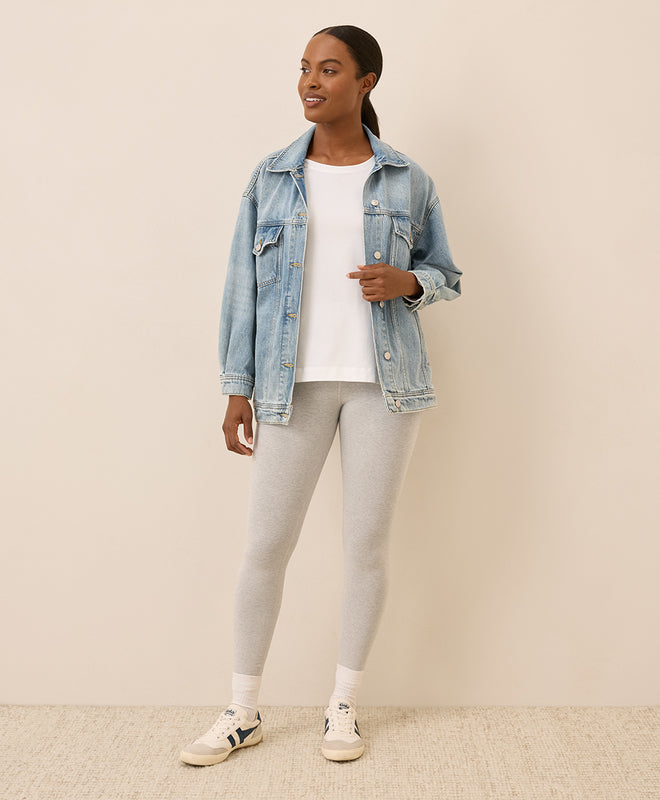 Woman wearing a denim jacket, white t-shirt, gray leggings, and white sneakers on a beige background
