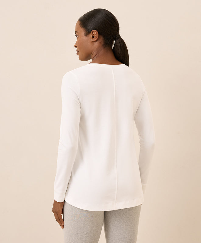 Woman wearing a white long-sleeve top against a beige background