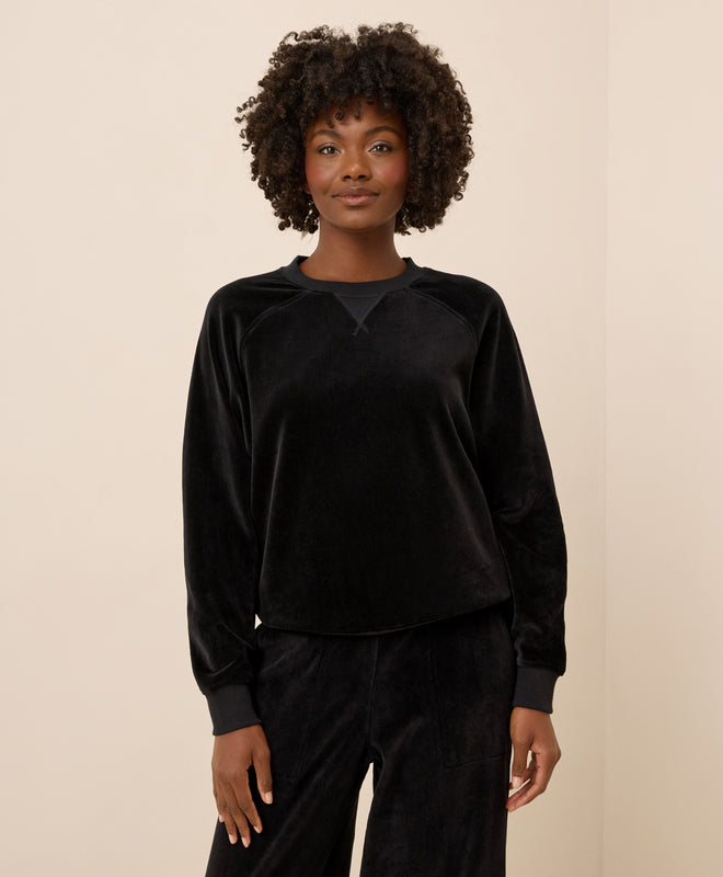Women wearing a black velour sweatshirt and pants on a beige background