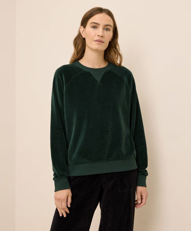 Woman wearing a dark green velour sweater against a beige background
