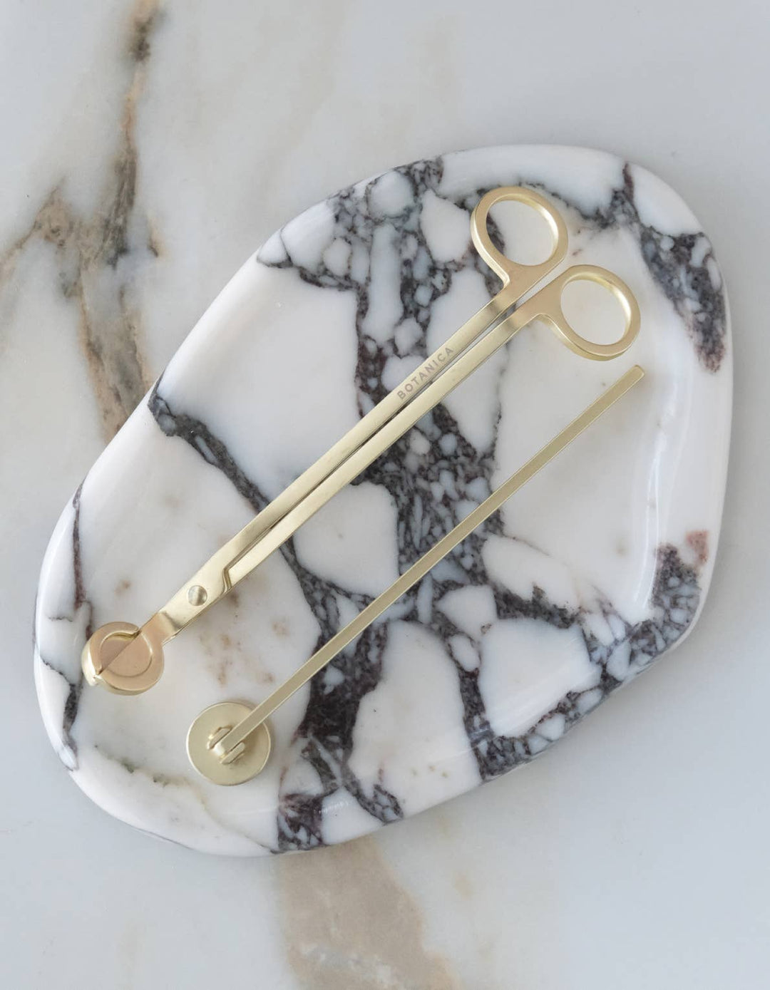Matte brass wick snipper and candle snuffer on a marble surface