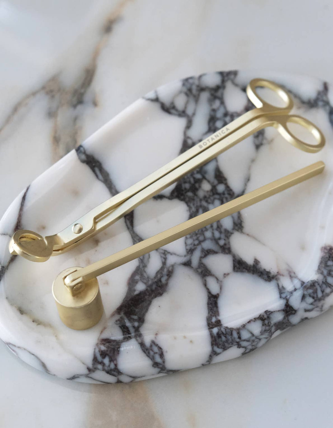 Matte brass snuffer and wick snip on a marble surface