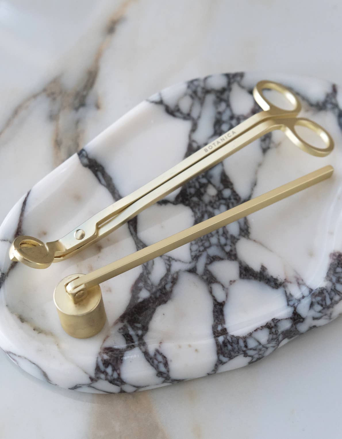 Matte brass snuffer and wick snip on a marble surface