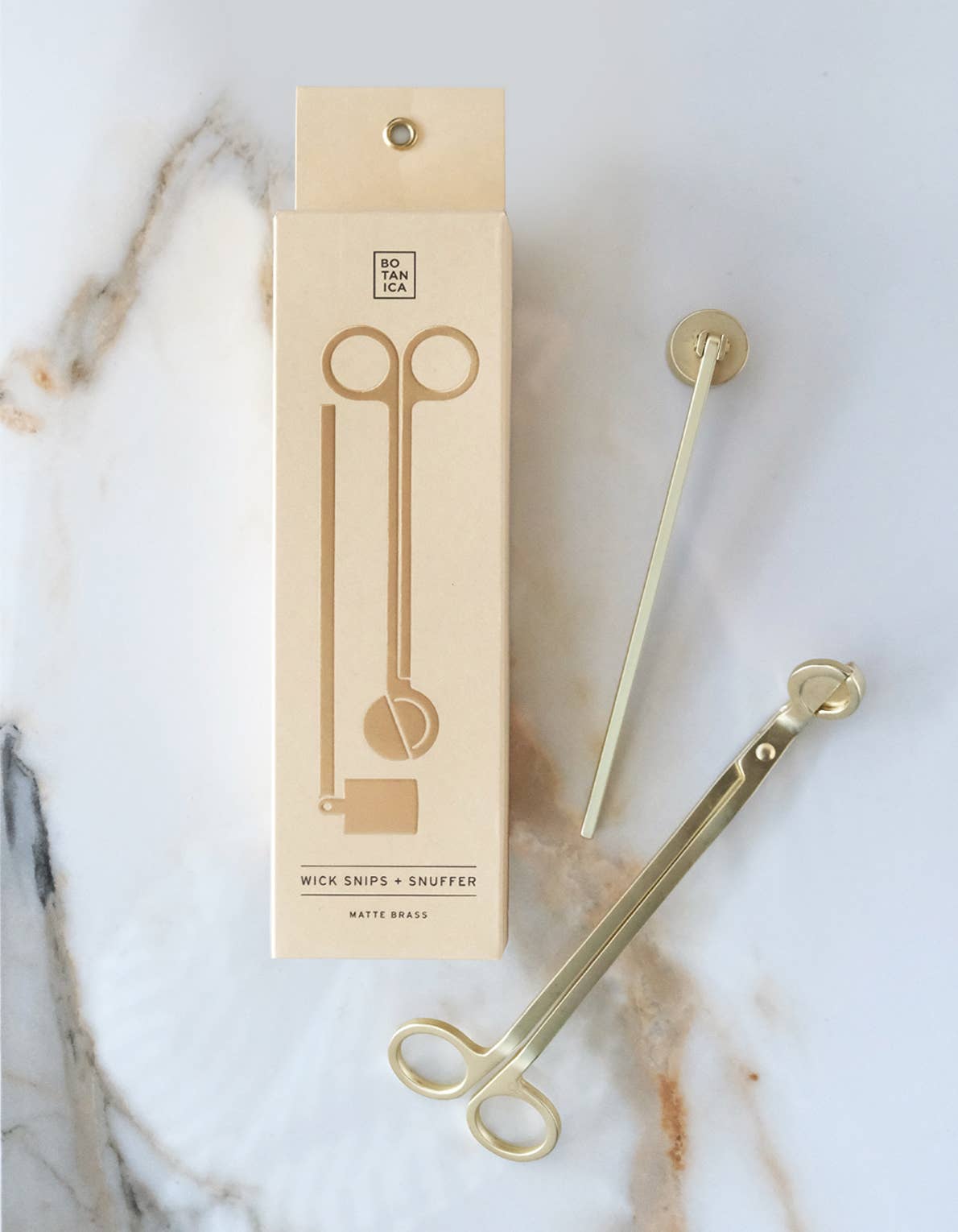 Matt brass wick snips and snuffer set with packaging on a marble surface