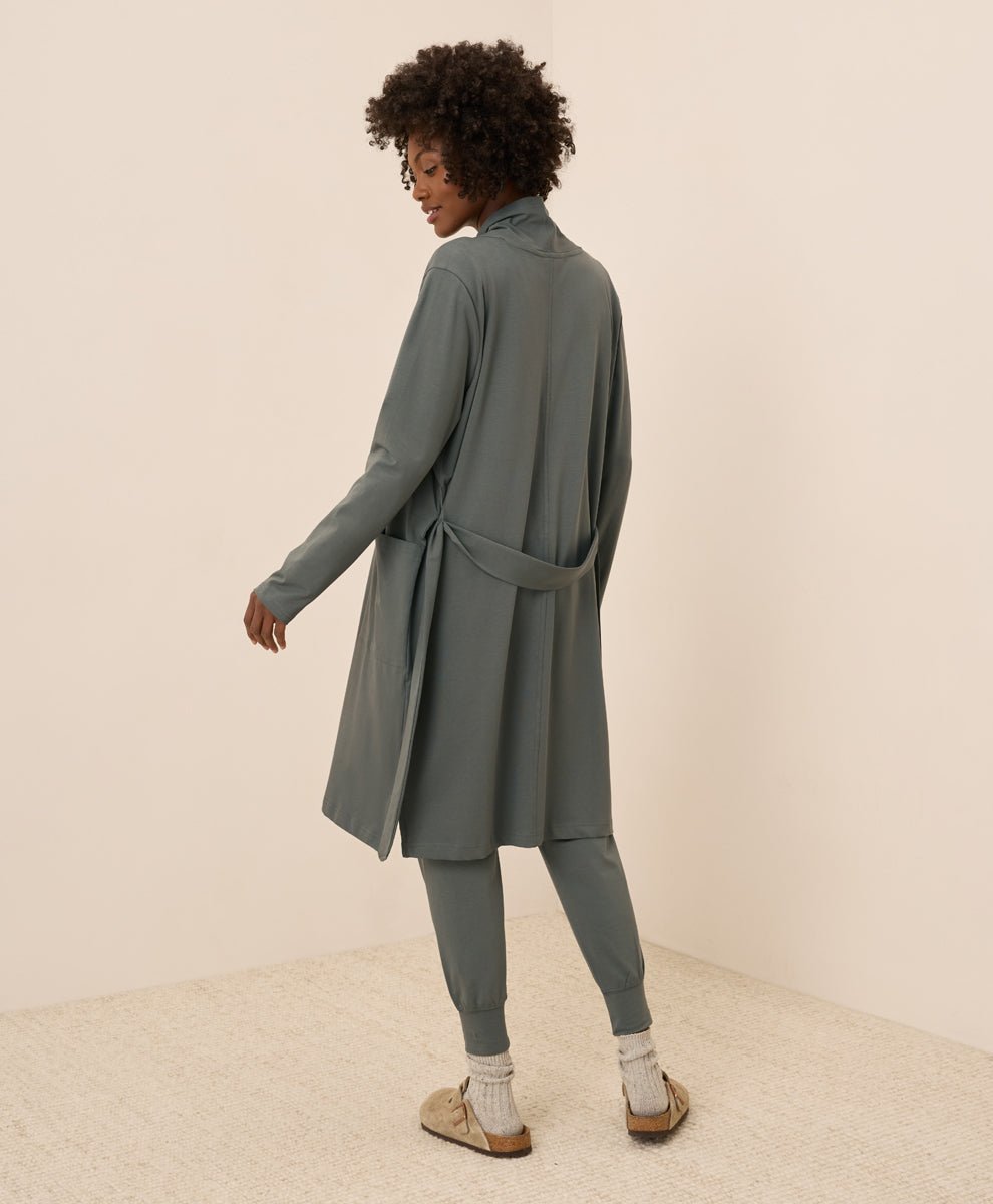 Person wearing a long, castor green duster with a belt on a plain background
