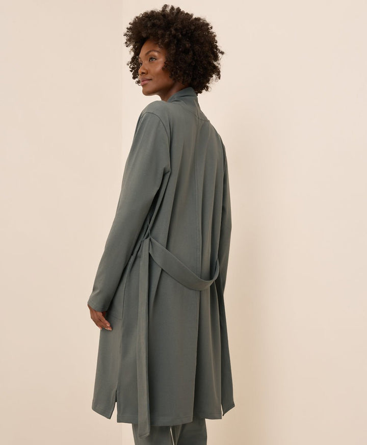 Woman wearing a long, castor green duster against a beige background