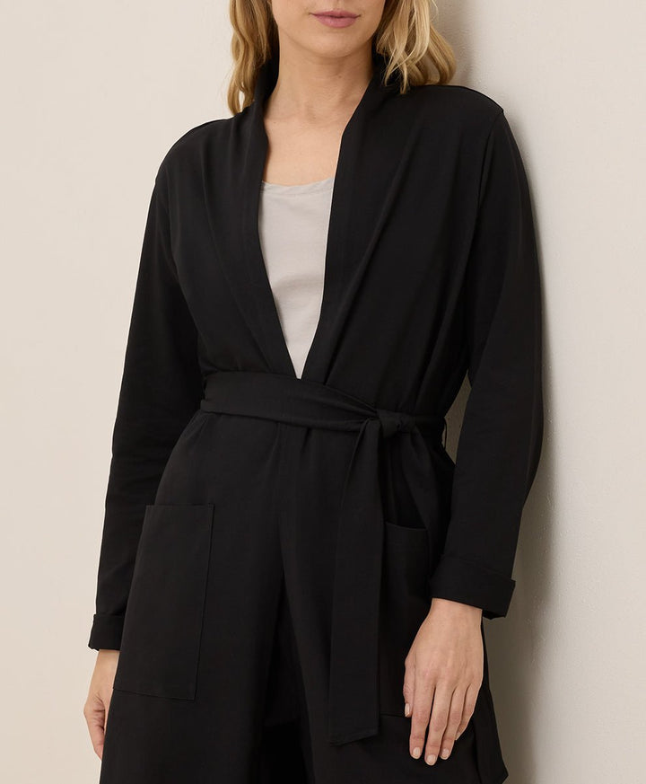 Woman wearing a black belted outfit against a beige background