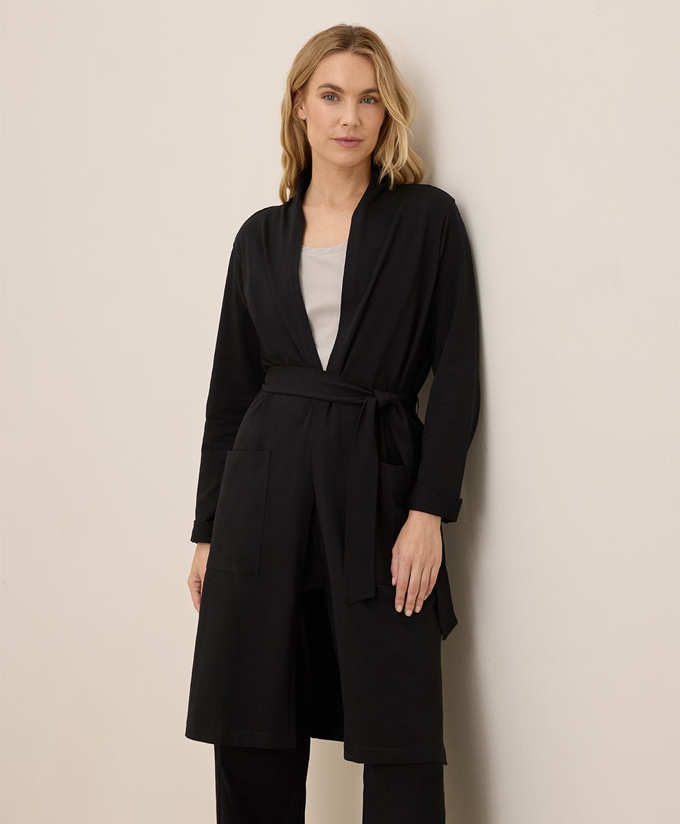 Woman wearing a black duster against a beige wall