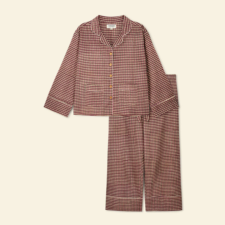 A two-piece pajama set featuring a long-sleeve button-front top and matching wide-leg pants in a fine red and beige gingham check pattern, laid flat on a light cream background.