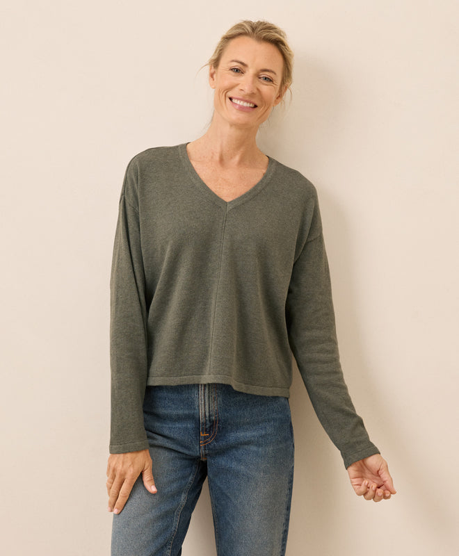 Woman wearing a green sweater and blue jeans against a beige background