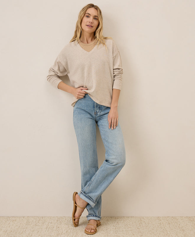 Woman wearing a beige sweater and blue jeans against a plain background