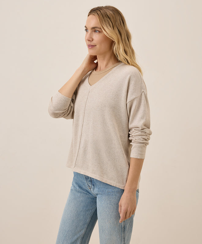 Woman wearing a beige sweater and blue jeans against a plain background