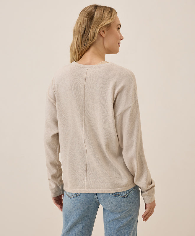 Woman wearing a beige sweater and blue jeans against a plain background