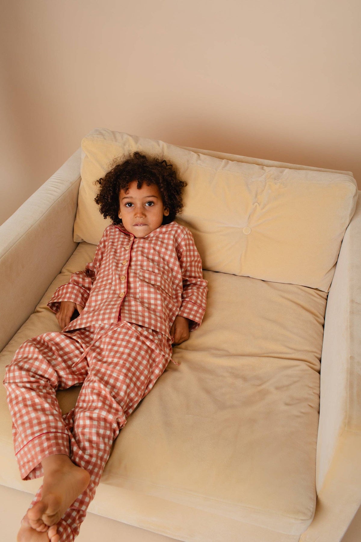 Child in red checkered pajamas lying on a beige couch with a neutral background